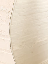 Load image into Gallery viewer, A close-up of a large oval mirror with a thin dark border, reflecting a warm off-white brick wall.

