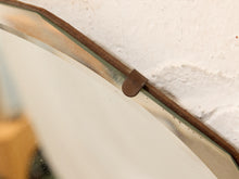 Load image into Gallery viewer, Close-up of a vintage-style mirror with a rusted brown metal frame and a small metal bracket, set against a textured off-white wall.
