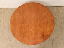 Load image into Gallery viewer, A round wooden table top with a warm orange-brown cherry wood grain finish, shown from a top-down perspective on a beige woven rug.
