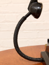 Load image into Gallery viewer, A close-up of a vintage black rotary telephone showing the coiled cord and handset against a light brick wall background.
