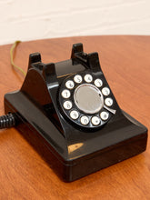 Load image into Gallery viewer, A vintage black rotary telephone with white-numbered buttons, resting on a wooden tabletop against a light brick wall.
