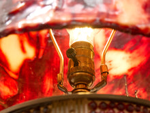 Load image into Gallery viewer, Close-up of a vintage-style lamp with a glowing light bulb, a brass-toned central socket, and a red marbled translucent shade or background.
