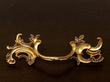 Load image into Gallery viewer, Vintage brass-tone furniture drawer pull with ornate scrolling Rococo-style backplates and curved handle
