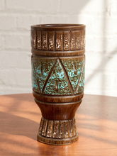 Load image into Gallery viewer, A ceramic goblet with a textured brown glaze and turquoise blue speckled bands, sitting on a wooden table against a white brick wall.
