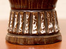 Load image into Gallery viewer, Close-up detail of a ceramic vessel base with a dark brown and white speckled glaze, set on a wooden surface.

