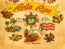 Load image into Gallery viewer, A close-up of a light wood surface featuring colorful Puerto Rico-themed artwork, including a yellow banner reading 'Puerto Rico,' the Puerto Rican coat of arms, a waving Puerto Rican flag, tropical palm trees, mountains, and fruit.
