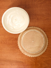 Load image into Gallery viewer, A white ceramic bowl filled with whipped cream sits next to a round, unglazed beige ceramic plate on a warm brown wooden tabletop.
