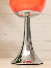 Load image into Gallery viewer, A close-up of a table lamp with a glossy orange-red spherical shade and a polished chrome flared base, shown against a light wood background.
