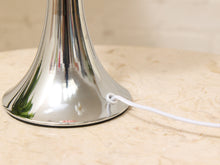 Load image into Gallery viewer, Close-up of a polished silver metal table lamp base on a beige marble surface, with a white power cord extending to the right.
