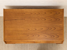 Load image into Gallery viewer, A top-down view of a rectangular wooden cabinet or desk with a warm medium-brown wood grain finish, positioned against a white brick wall and light beige woven rug.
