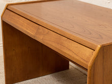 Load image into Gallery viewer, A close-up of a mid-century modern wooden desk with a warm honey-brown finish, featuring a slanted top, a front drawer, and a visible wood grain pattern.
