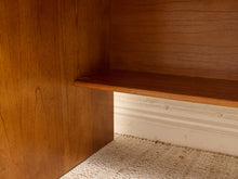 Load image into Gallery viewer, Close-up of a warm medium-brown wooden shelf unit with a single shelf, set against a white baseboard and light beige woven carpet.
