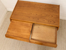 Load image into Gallery viewer, A mid-century modern wooden nightstand with a warm honey-toned wood grain finish, featuring one closed drawer and one open drawer, set against a white brick wall and light beige carpet.
