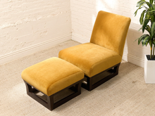 Load image into Gallery viewer, A mustard yellow velvet lounge chair with a matching ottoman, both featuring dark wood bases, set in a bright room with a white brick wall and a potted plant.
