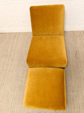 Load image into Gallery viewer, A mustard yellow velvet lounge chair with a matching ottoman, set on a textured beige rug against a white brick wall.
