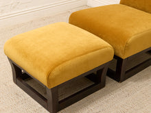 Load image into Gallery viewer, Two square ottomans upholstered in mustard yellow velvet fabric with dark brown wooden frames, shown on a textured beige carpet.
