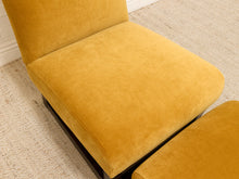 Load image into Gallery viewer, A close-up of a mustard yellow velvet upholstered armchair with a matching ottoman, set on a textured beige rug.
