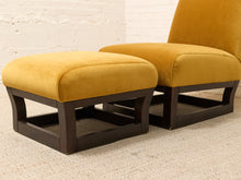 Load image into Gallery viewer, A mustard yellow velvet ottoman and matching accent chair with dark wood frames, set against a white brick wall and light beige carpet.
