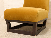 Load image into Gallery viewer, A mustard yellow velvet upholstered accent chair with a dark brown wooden frame, shown on a light beige carpet against a white brick wall.
