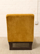 Load image into Gallery viewer, A mustard yellow velvet upholstered chair with a dark brown wooden base, photographed against a white brick wall and light beige rug.
