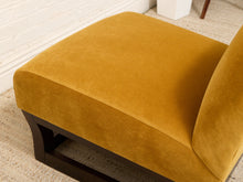 Load image into Gallery viewer, A mustard yellow velvet chaise lounge chair with a dark wood base, shown in a close-up view highlighting the soft fabric texture and the corner of the seat.
