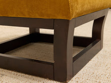 Load image into Gallery viewer, Close-up detail of an upholstered ottoman or bench with a mustard yellow velvet seat and a dark brown wooden frame on a beige textured rug.
