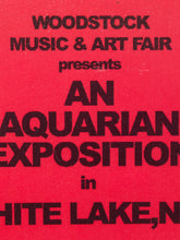 Load image into Gallery viewer, A vintage program cover or poster for the Woodstock Music &amp; Art Fair, featuring bold black text on a bright red background. The text reads 'WOODSTOCK MUSIC &amp; ART FAIR presents AN AQUARIAN EXPOSITION in WHITE LAKE, N.
