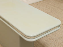 Load image into Gallery viewer, A close-up of a glossy pale sage green table or bench corner, showing the curved top edge and side panel, set on a beige carpeted floor.
