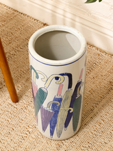 Load image into Gallery viewer, A cylindrical ceramic floor vase with a hand-painted umbrella pattern, sitting on a beige woven rug next to a wooden leg.
