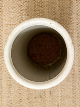 Load image into Gallery viewer, A top-down view of a white ceramic cup or small pot with a cork stopper inside, set against a textured beige woven fabric background.
