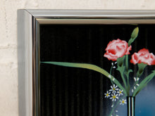 Load image into Gallery viewer, A close-up of a framed floral artwork showing pink flowers with green stems on a black background, set against a light textured wall.
