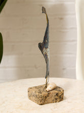 Load image into Gallery viewer, A small decorative sculpture featuring a tall, slender abstract metallic blade mounted on a rough stone base with a small shell accent, set on a light stone tabletop against a softly blurred indoor background.
