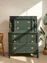 Load image into Gallery viewer, Antique hunter green highboy dresser with ornate carved details, turned columns, multiple drawers, and round brass-tone pulls

