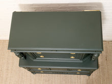Load image into Gallery viewer, An overhead view of a dark green three-drawer chest of drawers with brass handles, positioned against a white brick wall and beige rug.
