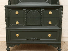 Load image into Gallery viewer, A dark forest green carved wooden chest of drawers with ornate gold drawer pulls, shown against a white brick wall background.
