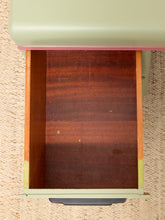 Load image into Gallery viewer, An open drawer of a vintage desk or cabinet, showing a dark brown wood interior, a sage green painted exterior, and a black metal pull handle, set against a beige woven rug.
