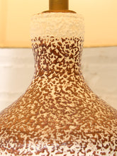 Load image into Gallery viewer, Close-up of a ceramic lamp base with a textured speckled glaze in brown and cream, featuring a brass-colored neck finial at the top.
