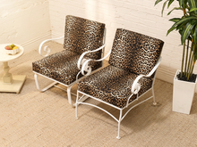 Load image into Gallery viewer, Two outdoor armchairs with white metal frames and leopard-print cushions, shown in a bright patio setting with a potted plant and side table.
