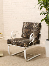Load image into Gallery viewer, A modern accent chair with a white metal frame and leopard-print cushions, set on a beige rug against a white brick wall with a potted plant nearby.

