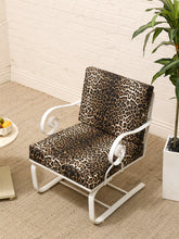 Load image into Gallery viewer, A modern accent chair with a white metal frame and leopard-print cushions, set on a beige carpet against a white brick wall next to a potted plant.
