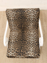 Load image into Gallery viewer, A leopard print cushion on a white rocking chair, set on a beige woven rug against a white brick wall.
