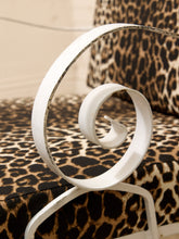 Load image into Gallery viewer, A white metal decorative scroll accent piece displayed on a leopard-print upholstered chair.
