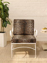 Load image into Gallery viewer, A white metal outdoor lounge chair with leopard-print cushions, set against a white brick wall with a potted plant and a small side table.
