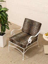 Load image into Gallery viewer, A white metal accent chair with leopard-print cushions, set on a beige jute rug against a white brick wall with a potted plant and side table nearby.

