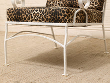 Load image into Gallery viewer, A close-up of a white metal lounge chair with leopard-print cushions, set on a beige textured rug against a white brick wall.

