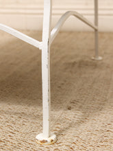 Load image into Gallery viewer, Close-up of a white metal table leg with distressed paint and a round base, standing on a beige woven rug.
