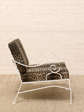 Load image into Gallery viewer, A white metal lounge chair with leopard-print cushions, set against a white brick wall and a beige woven rug.
