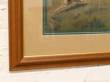 Load image into Gallery viewer, A close-up of a framed art print featuring a hunting dog in a grassy field, mounted on a white brick wall. The frame is a warm medium brown wood with a twisted rope pattern, surrounded by a wide beige mat and a thin green inner border.
