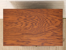 Load image into Gallery viewer, A rectangular wood panel with a prominent wavy grain pattern in warm reddish-brown tones, displayed flat against a white brick wall and beige woven floor.
