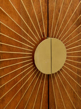 Load image into Gallery viewer, A close-up of a round brass door handle mounted on a wooden door with a sunburst inlay pattern.
